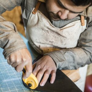 Tailor using rotary cutter on fabric on workshop bench